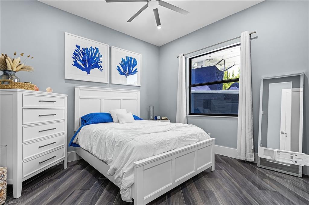 Bedroom featuring wood-finish flooring, a contemporary ceiling fan with integrated lighting, and a large window with white curtain rods