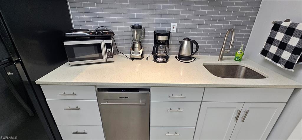 White cabinetry with modern hardware, light-toned countertop, stainless steel sink with high-arc faucet, subway tile backsplash, and stainless steel dishwasher