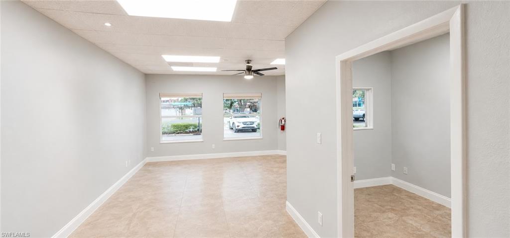 Spacious interior room featuring light-colored walls, tile flooring, and multiple windows