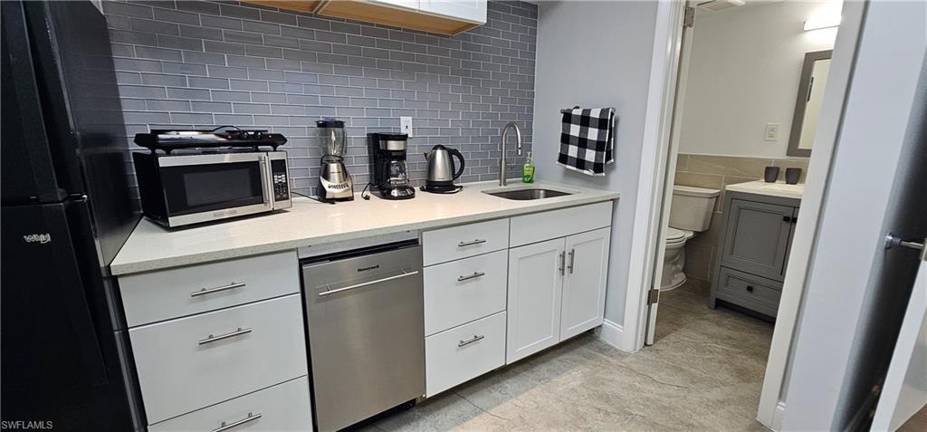 Compact kitchen area featuring a stainless steel dishwasher, white cabinetry, and a light-colored countertop