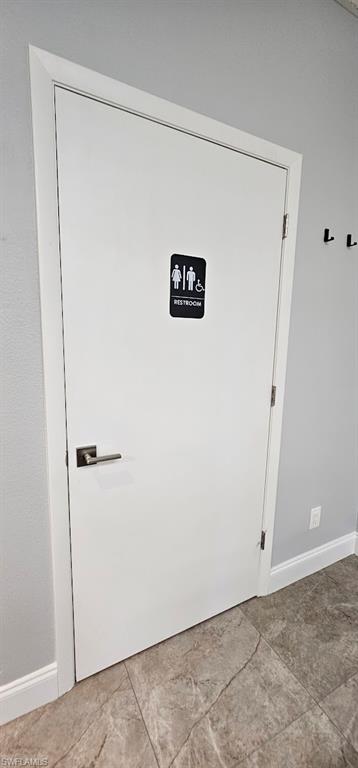 White interior door with contemporary hardware, light gray walls, white baseboards, and large format floor tile