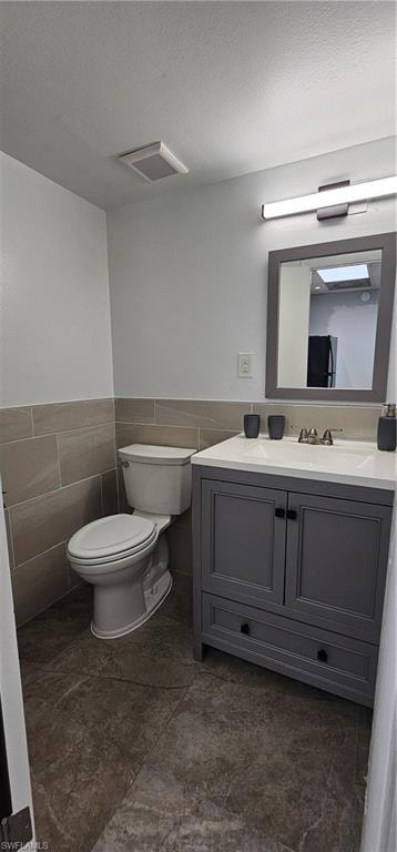 Gray vanity with a white countertop and integrated sink, framed mirror, wall-mounted light fixture, and tile flooring