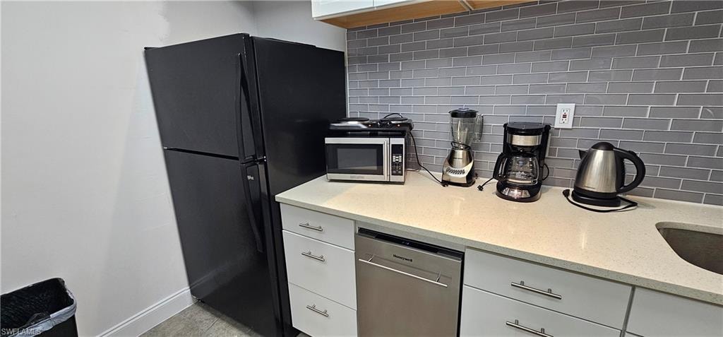 Kitchenette featuring a black refrigerator, stainless steel dishwasher, light-toned countertop, and gray subway tile backsplash