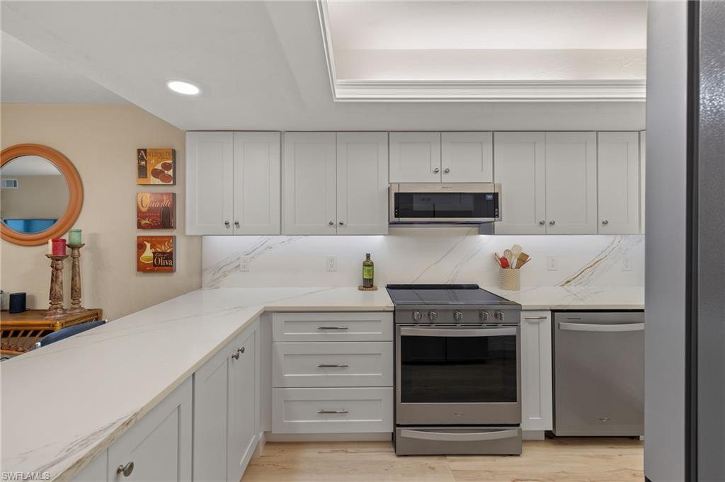 Kitchen with white cabinets, decorative backsplash, light hardwood / wood-style floors, light stone counters, and stainless steel appliances