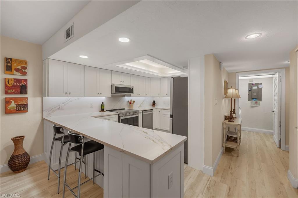 Kitchen with kitchen peninsula, appliances with stainless steel finishes, a breakfast bar, light hardwood / wood-style floors, and white cabinetry