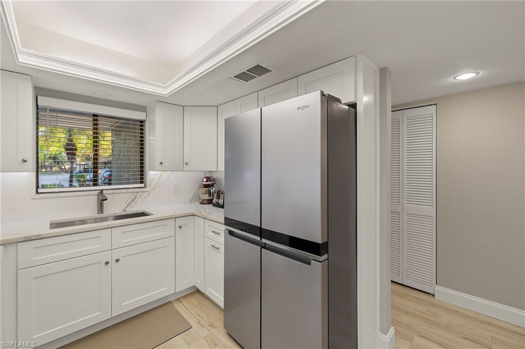 Kitchen with white cabinets, stainless steel fridge, light hardwood / wood-style floors, and sink