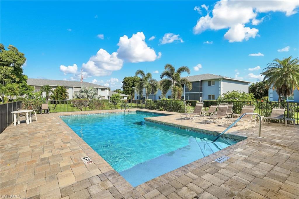 Outdoor swimming pool with integrated shallow entry, surrounded by paver decking, and secured by a perimeter fence