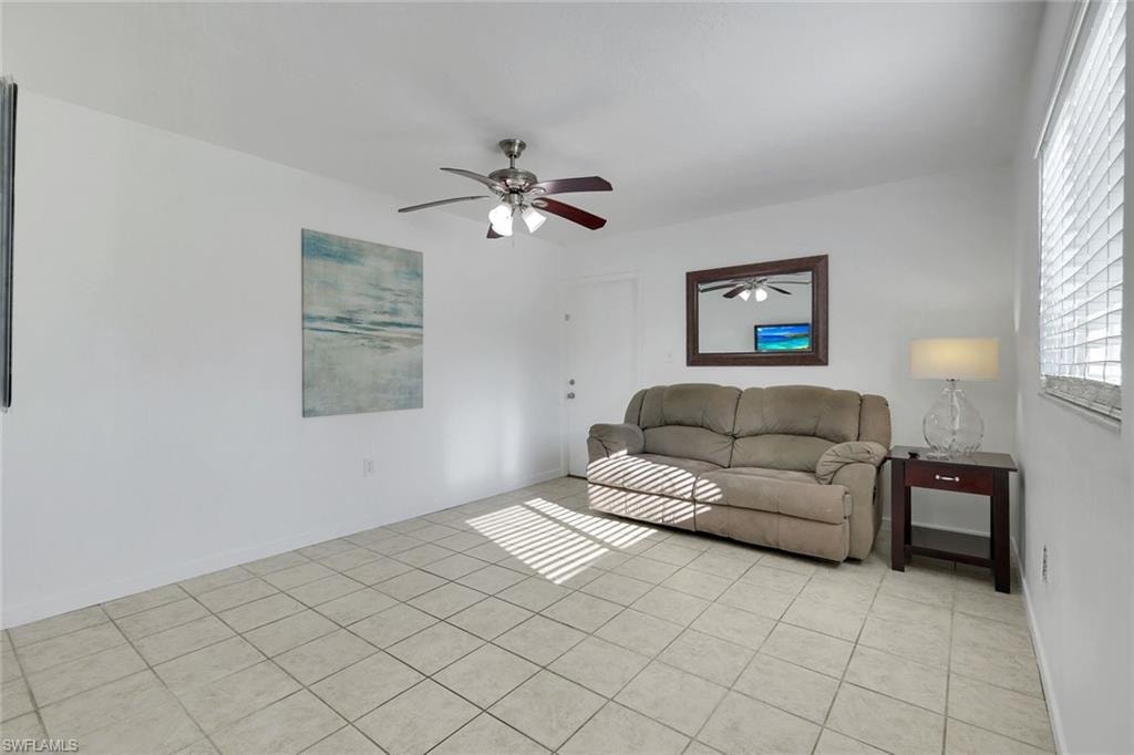 Bright, open living space showcasing tile flooring throughout, ceiling fan with integrated lighting, and abundant natural light from expansive windows