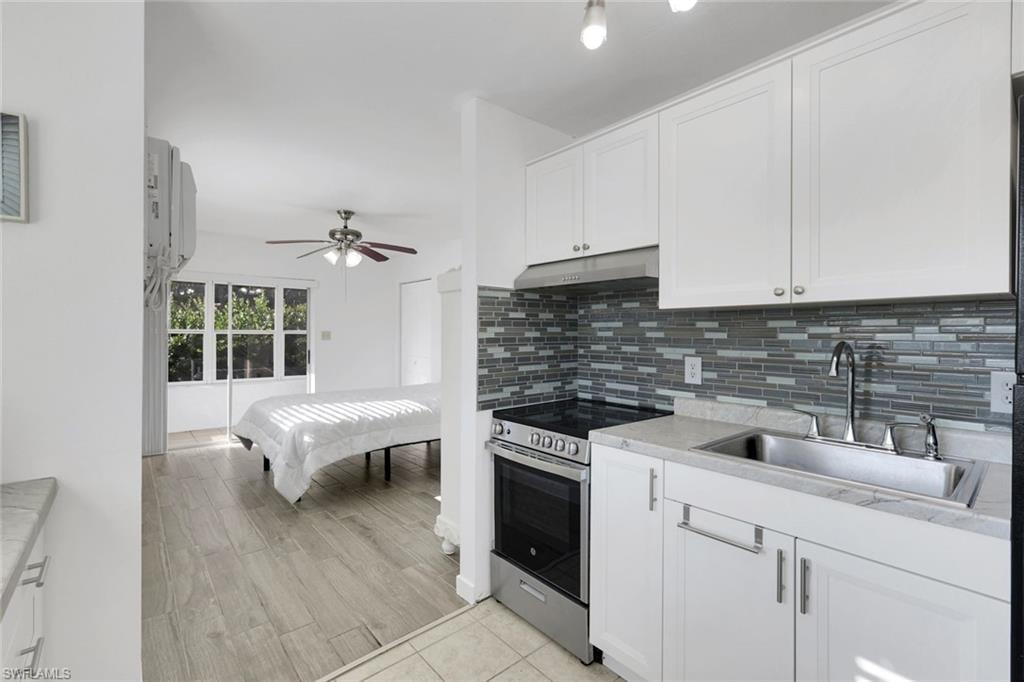 Open-concept kitchen and bedroom featuring white cabinetry with brushed nickel hardware, stainless steel appliances including a gas range, subway tile backsplash, white quartz countertops, and wood-finish flooring throughout