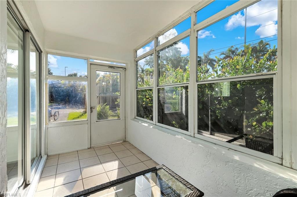 Bright sunroom with expansive fixed-window glazing offering natural light and outdoor vistas, ceramic tile flooring, and multiple glass sliding doors providing access to the exterior grounds