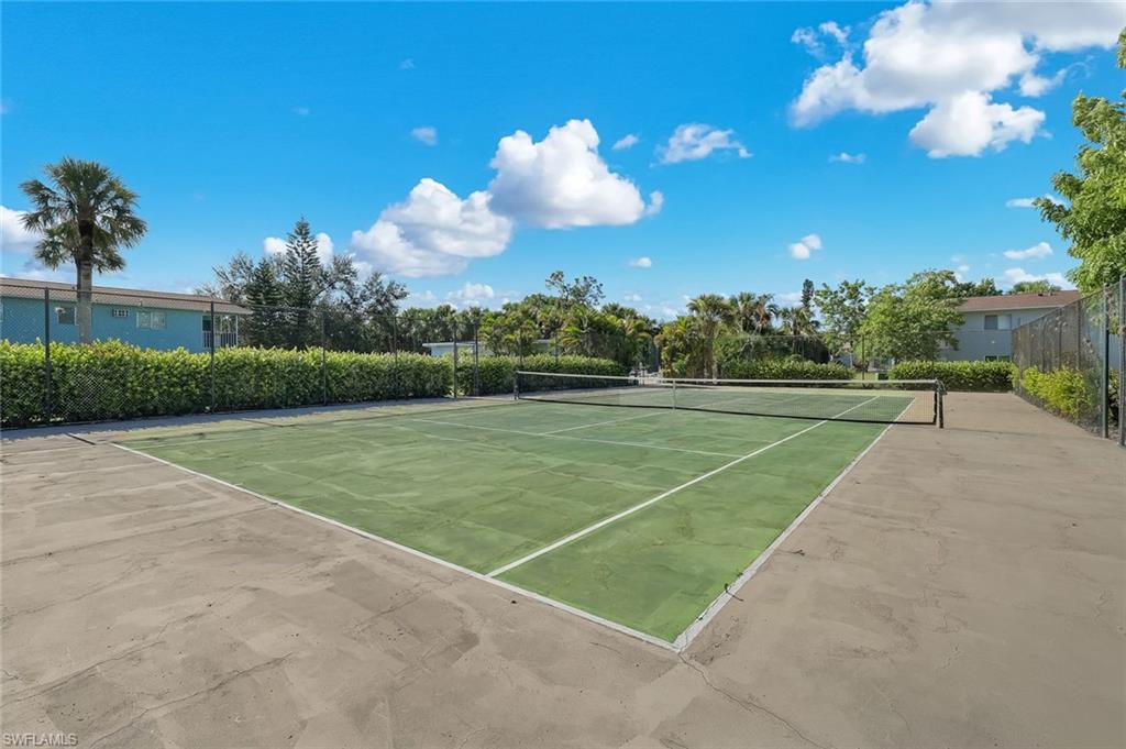 Tennis court with green surface, surrounding concrete perimeter, and chain-link fencing
