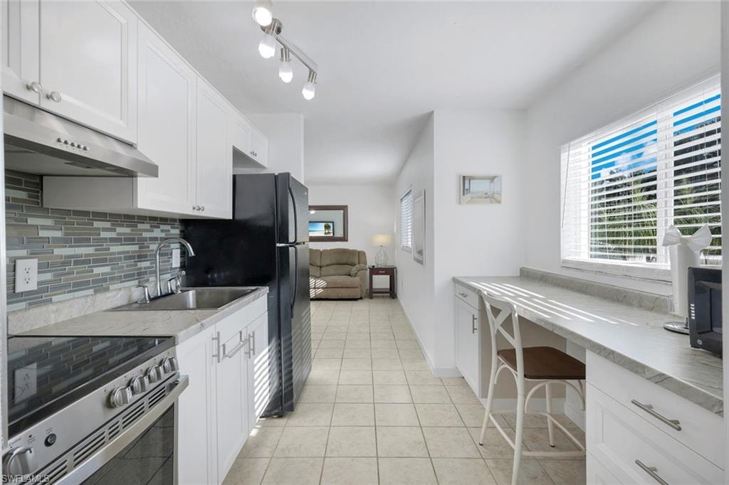 Kitchen featuring white cabinetry, a tile backsplash, stainless steel range with hood, and a built-in breakfast bar