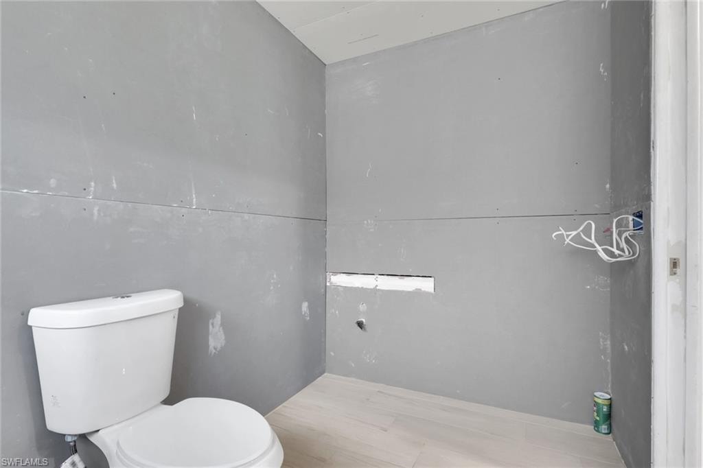 Powder room featuring a white two-piece toilet, light wood-finish flooring, and unpainted drywall walls