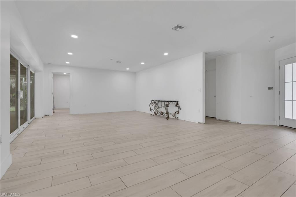 Spacious room featuring light-toned plank flooring, white walls, recessed ceiling lighting, and expansive glass panel doors opening to the exterior