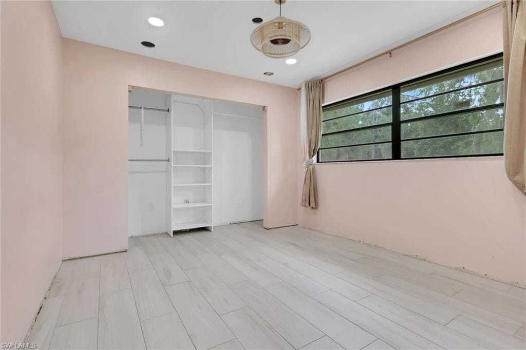 Interior space featuring light-toned wood-finish flooring, a built-in closet with shelving and hanging rods, a window with exterior visibility, recessed ceiling lighting, and a central ceiling light fixture