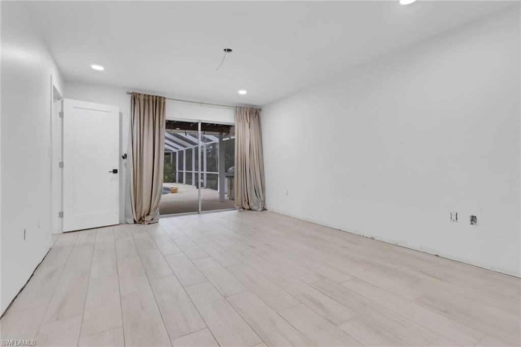 Spacious interior with light-tone wood-finish flooring, recessed ceiling lighting, and a sliding glass door opening to a screened outdoor area with a pool