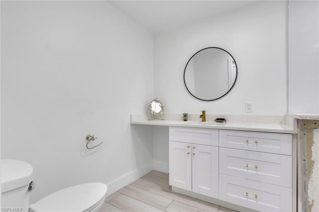 Bathroom featuring a white vanity with gold hardware, a circular wall-mounted mirror, a gold-finish faucet, a white countertop, and wood-finish tile flooring