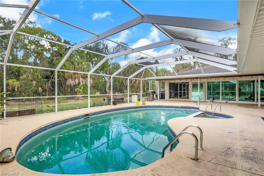 Expansive screened pool enclosure featuring a kidney-shaped pool with integrated spa and surrounding concrete decking