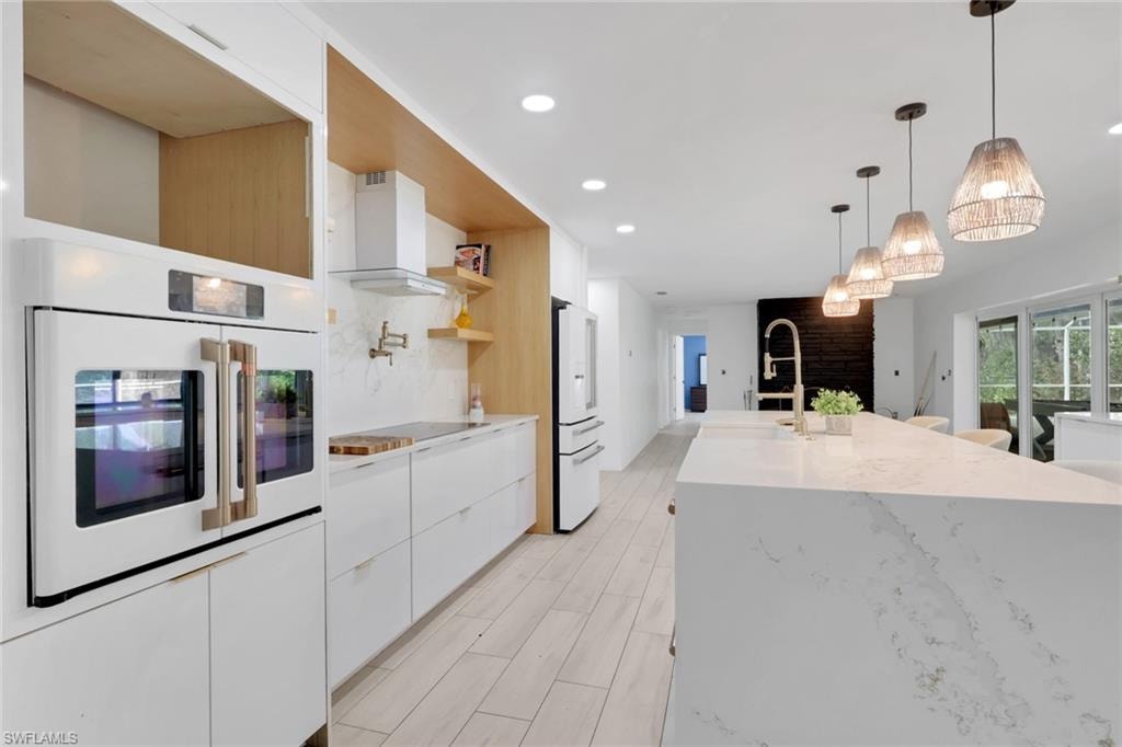 Modern kitchen featuring a double wall oven, white cabinetry, integrated range hood, wood-finish flooring, and a large central island with pendant lighting