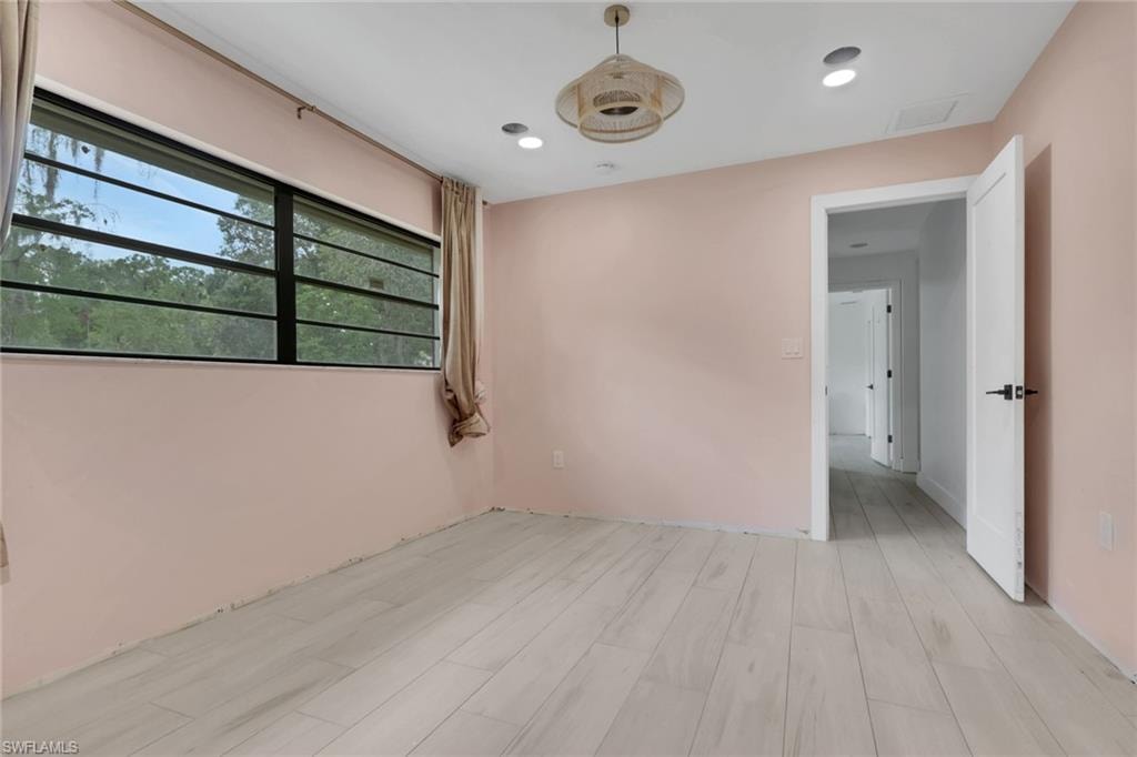 Spacious room featuring light wood-finish flooring, a large window with horizontal grilles, a contemporary ceiling fixture, recessed lighting, and a white interior door with matte black hardware