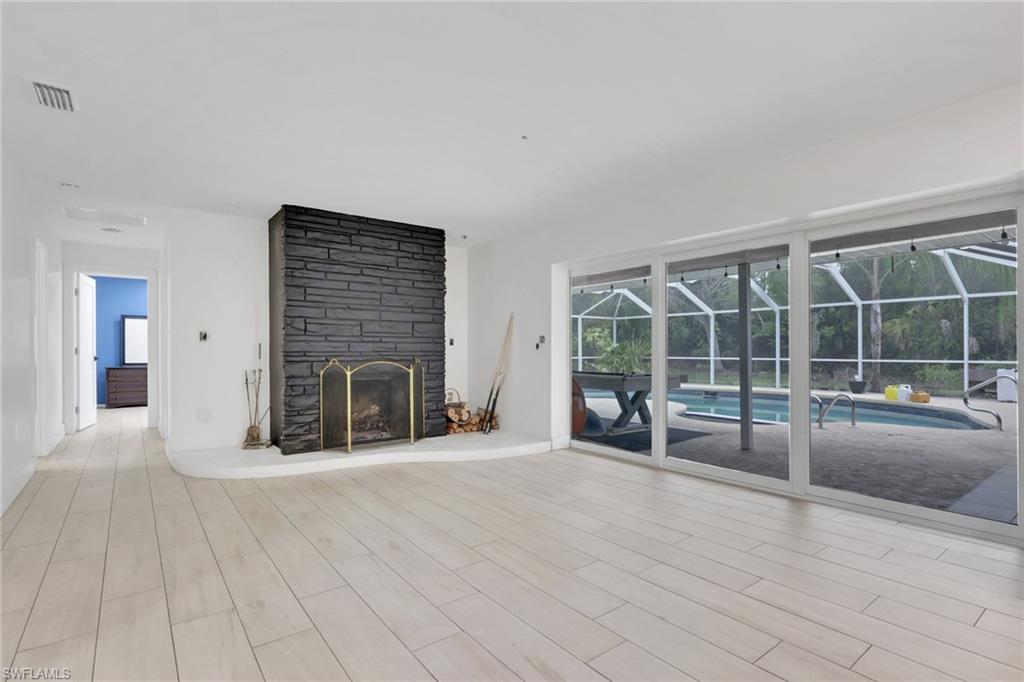Spacious room featuring light wood-finish flooring, a stacked stone fireplace with a white hearth, and expansive sliding glass doors