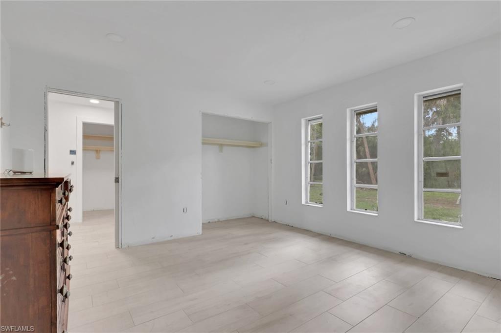 Spacious room featuring light-toned tile flooring, three large windows, a generous closet with shelving, and an additional doorway opening to another space