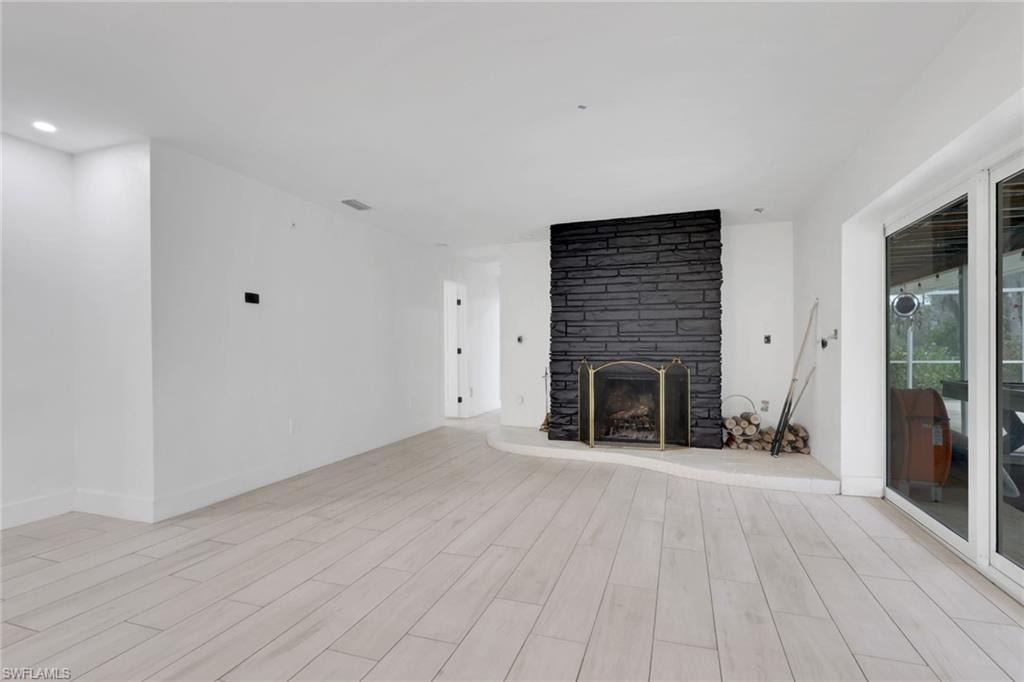 Spacious room featuring light wood-finish flooring, a prominent black stone-clad fireplace, and recessed ceiling lighting