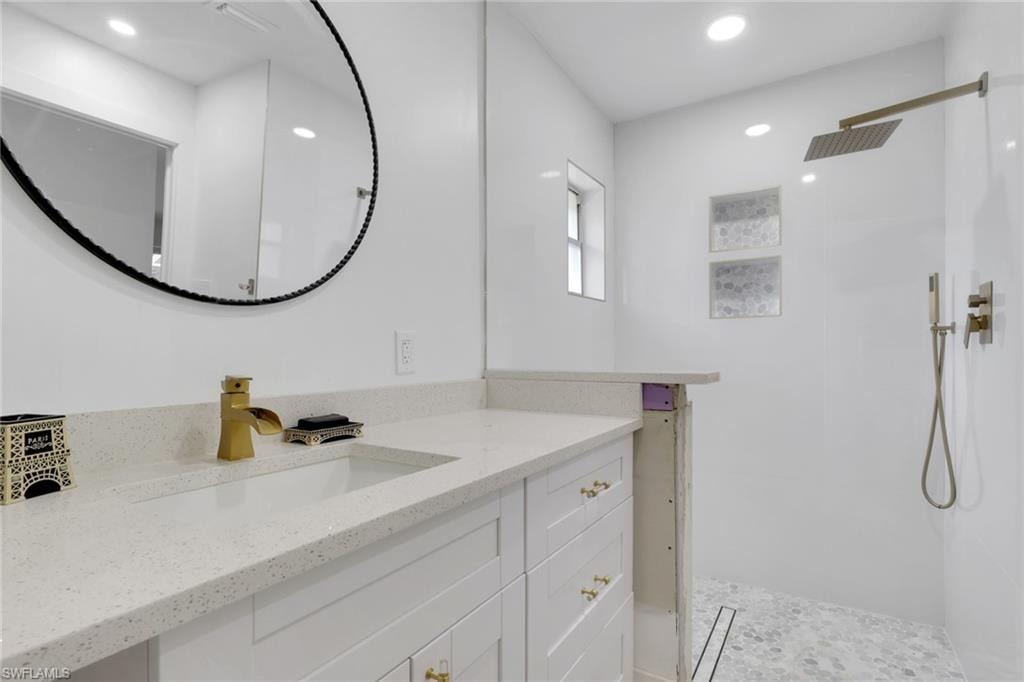 White vanity with a light speckled countertop, undermount sink, and brass-finish faucet