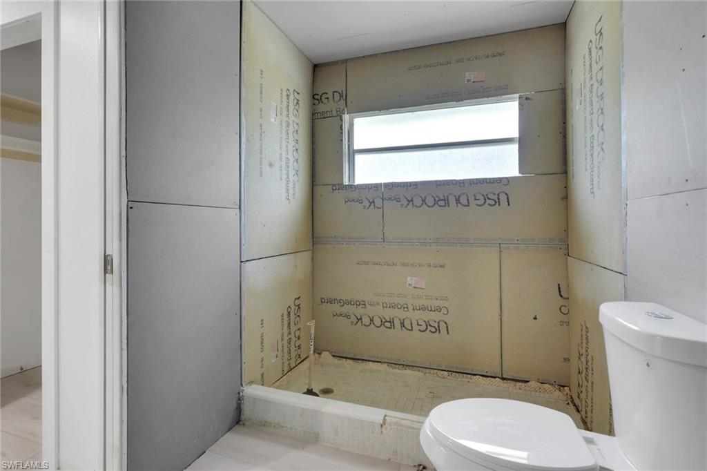 Bathroom under construction featuring cement board installation, a built-in shower niche, a window with frosted glass, and a white toilet fixture