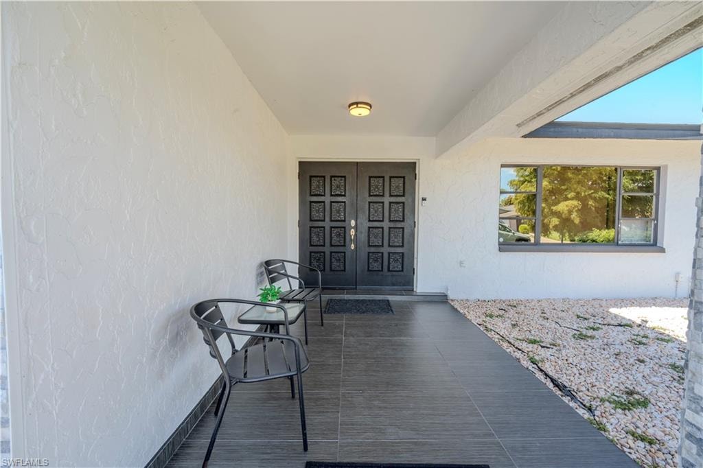 Covered entry with dark tile flooring, a double entry door, textured exterior wall, and integrated lighting