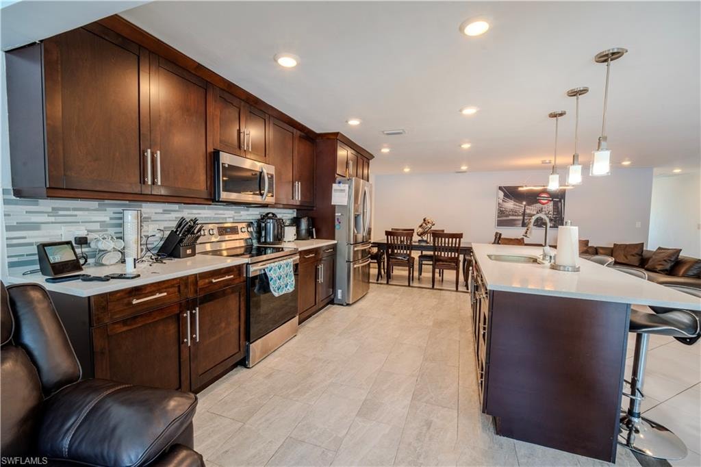 Kitchen featuring dark wood-finish cabinetry, stainless steel appliances, a mosaic tile backsplash, and light-toned countertops
