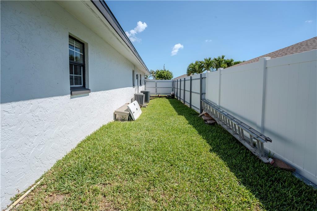 Side yard featuring a white stucco exterior, black-framed window, two exterior HVAC units, and a white privacy fence