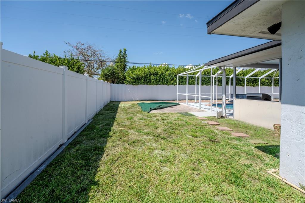 Private backyard featuring a white privacy fence, expansive lawn, and screened-in pool area with a covered patio