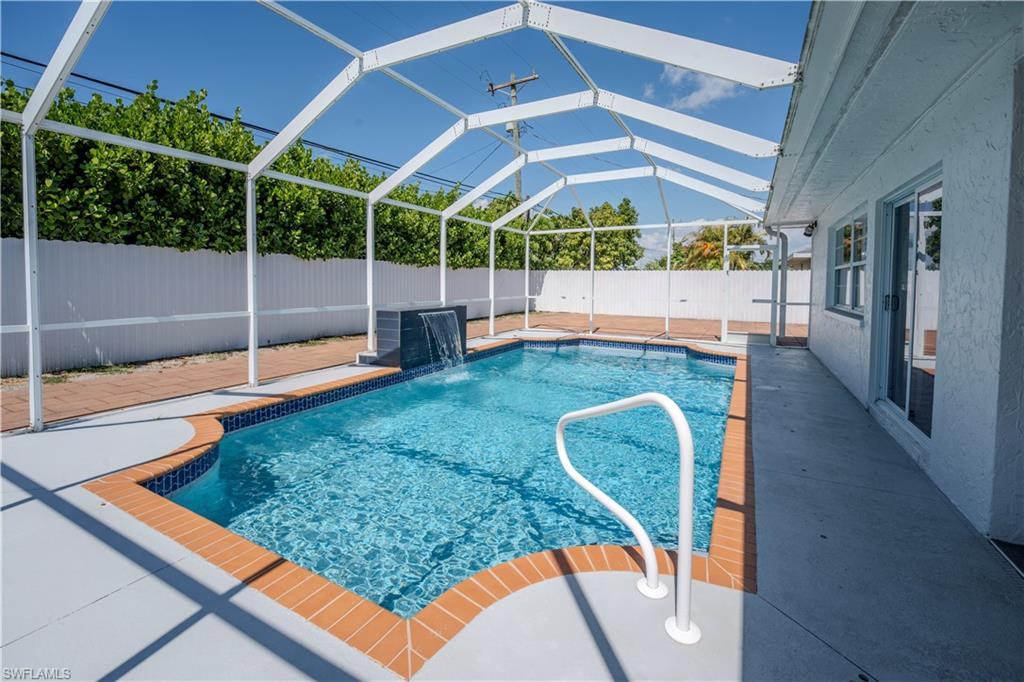Screen-enclosed swimming pool featuring a waterfall accent and brick coping