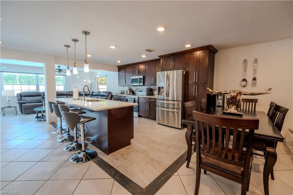 Spacious kitchen and dining area featuring dark wood cabinetry, stainless steel appliances, a center island with pendant lighting, and a dining table with matching chairs
