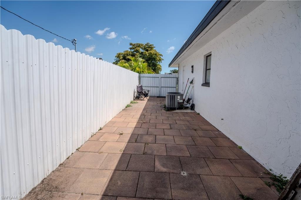 Paved side yard featuring a white corrugated fence and exterior stucco finish