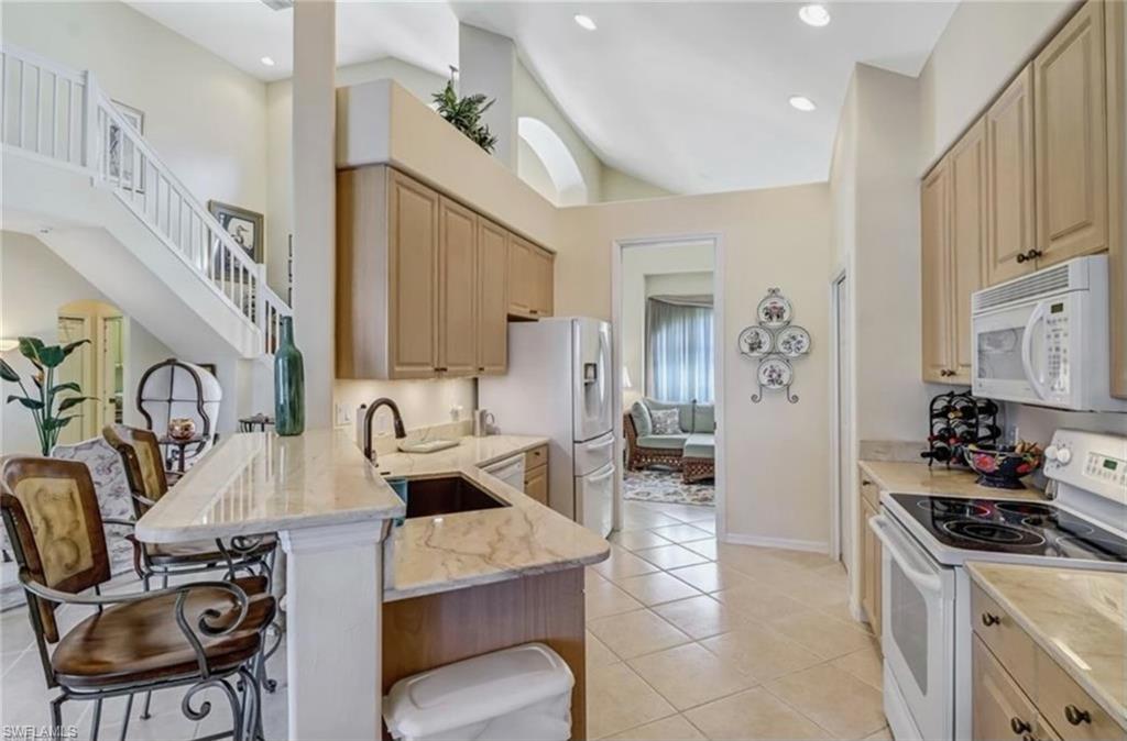 Kitchen featuring kitchen peninsula, white appliances, light tile patterned flooring, light brown cabinetry, and a breakfast bar area