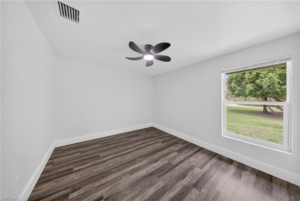 Bright interior space featuring a window with exterior scenery, dark wood-finish flooring, a ceiling fan with integrated lighting, white walls, and white baseboards