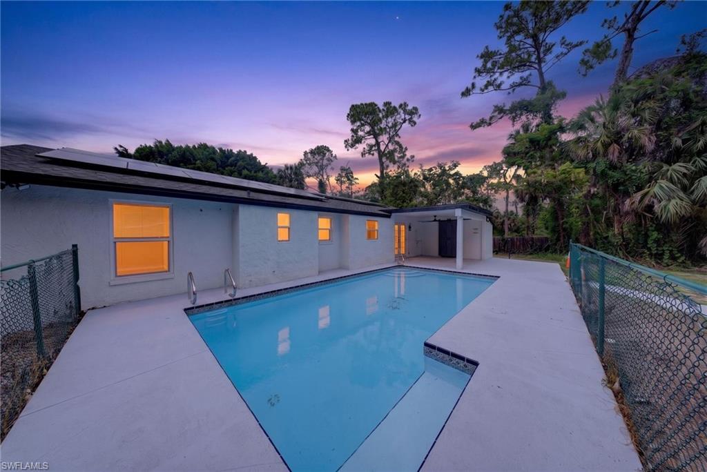 Outdoor swimming pool with concrete decking, a covered patio area, and mature trees in the background