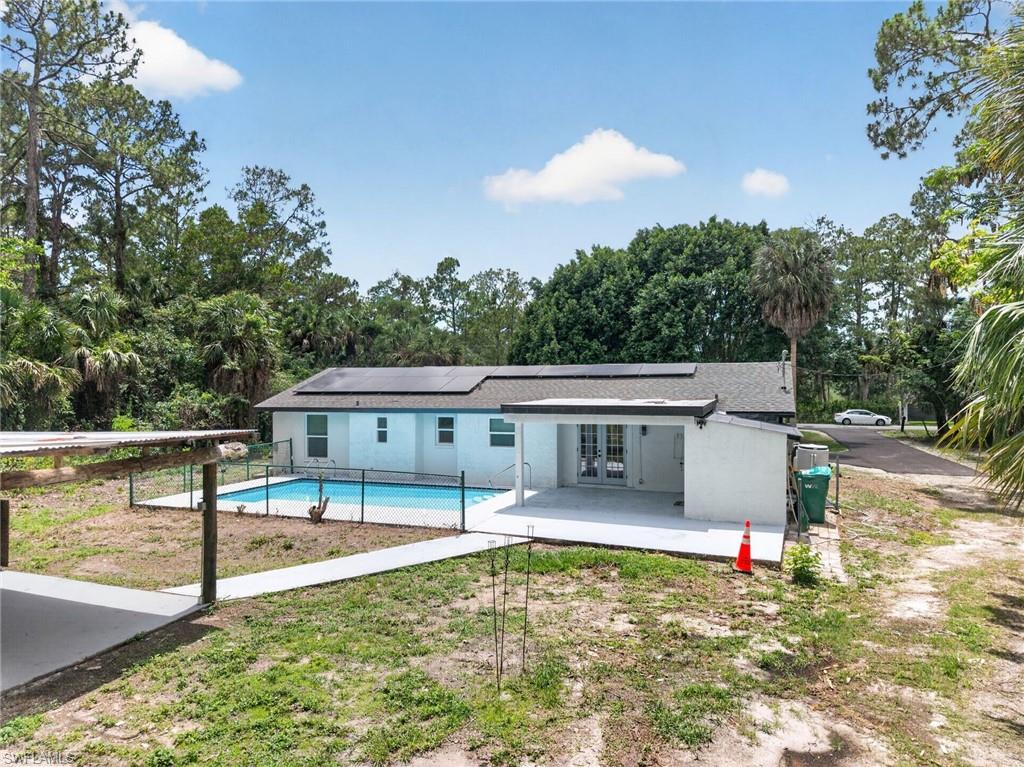 Residence featuring a private swimming pool with security fencing, an expansive patio, and solar panels on the roof