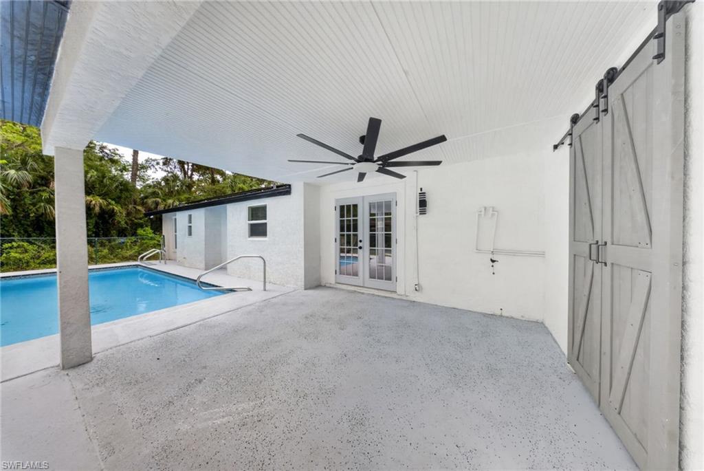 Covered patio with a large ceiling fan, concrete flooring, and double glass-paneled doors