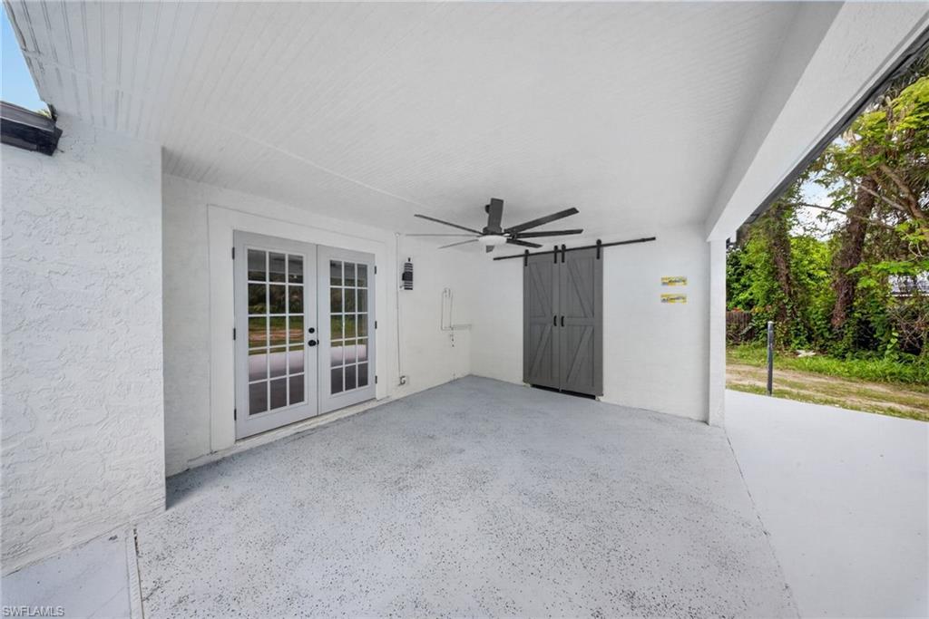 Covered patio featuring a ceiling fan, dual-pane French doors, a grey barn door, and a textured concrete floor