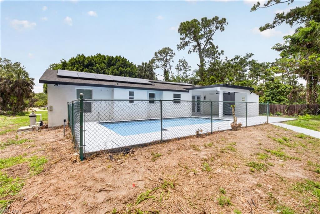 Rear exterior featuring a fenced swimming pool, covered patio, and solar panels