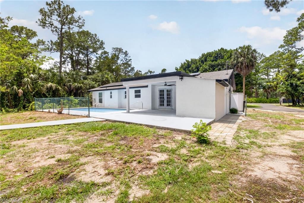 White stucco exterior with a covered patio, double French doors, and a fenced swimming pool