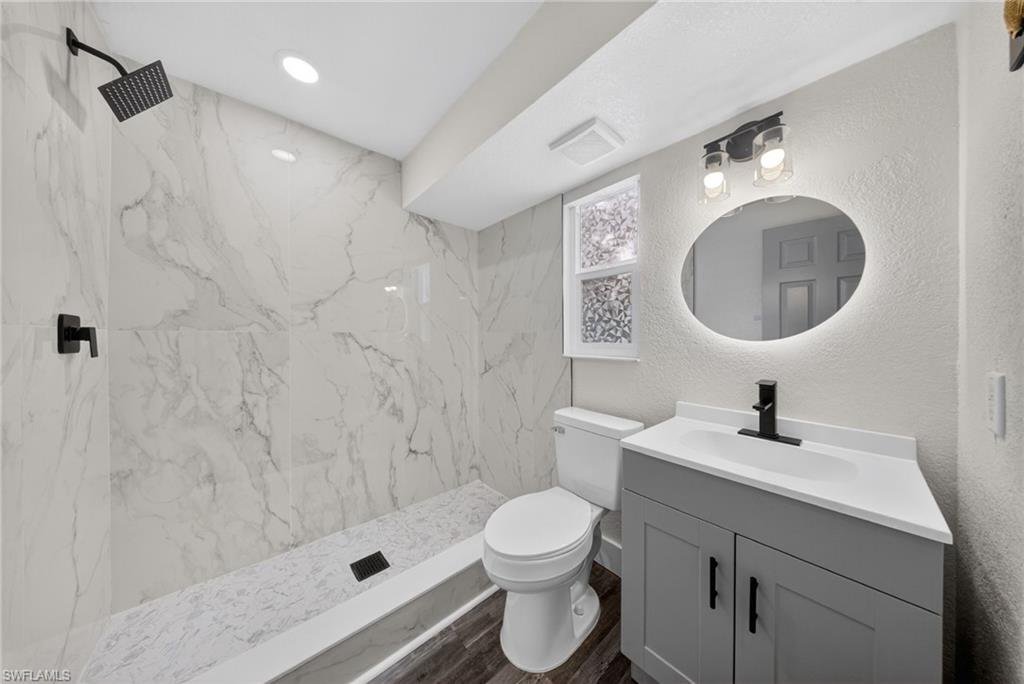 Bathroom featuring a walk-in shower with large format marble-look tile, matte black shower fixtures, a gray vanity with white countertop, and an illuminated oval mirror