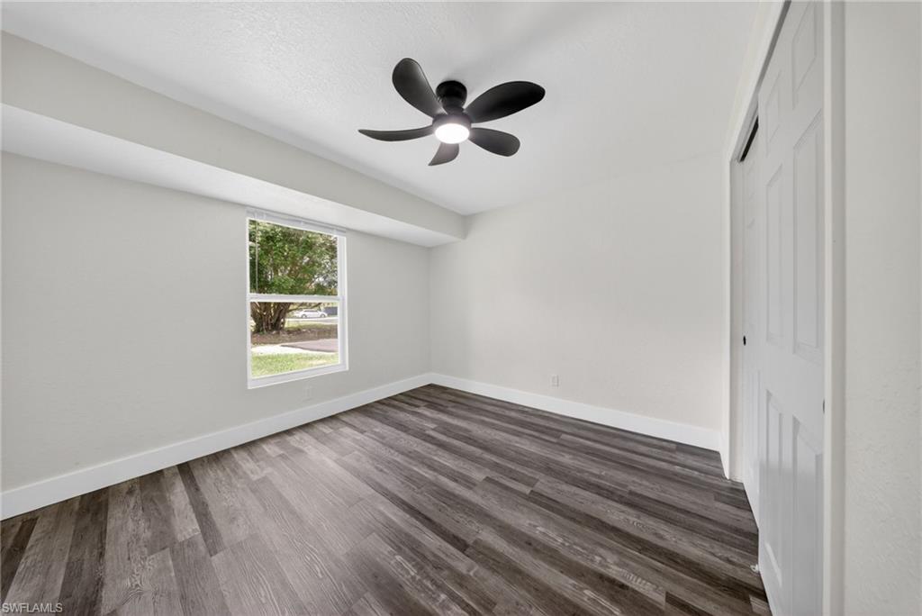 Room featuring wood-finish flooring, a window with outdoor landscaping, a ceiling fan with integrated lighting, and a bi-fold closet door