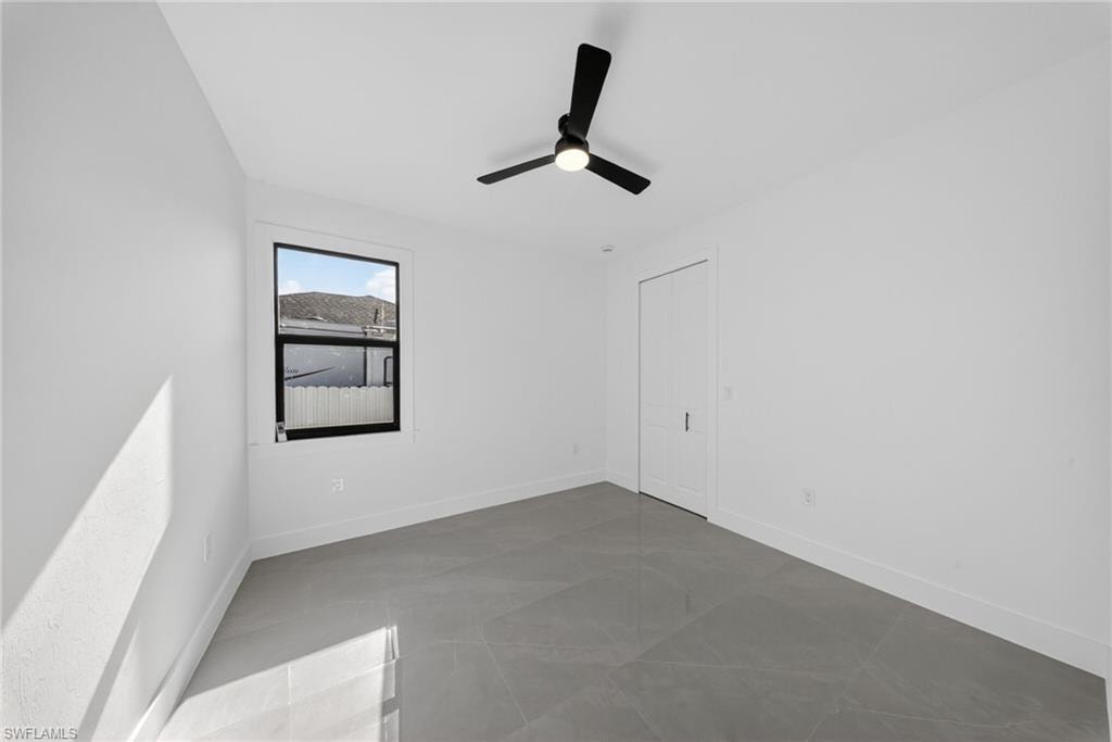 Light-filled room featuring a single window with black trim, a modern black ceiling fan, white walls, and large format grey tile flooring