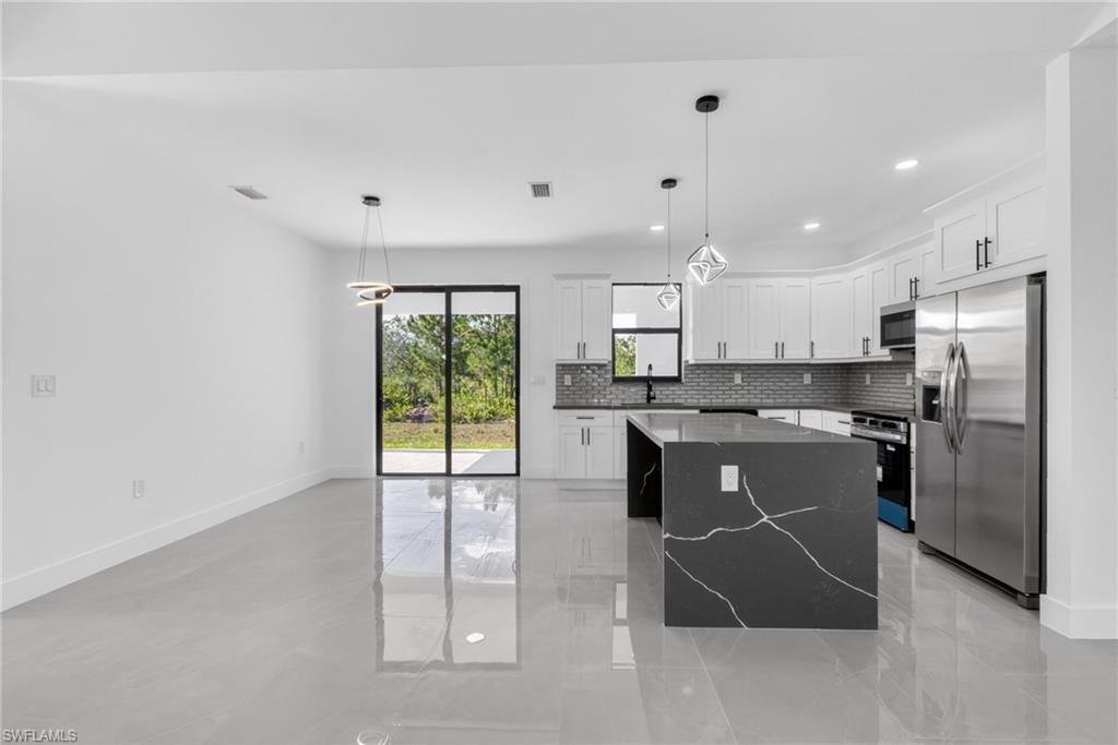 Contemporary kitchen featuring white cabinetry, a dark waterfall island with veining, stainless steel appliances, and a gray subway tile backsplash