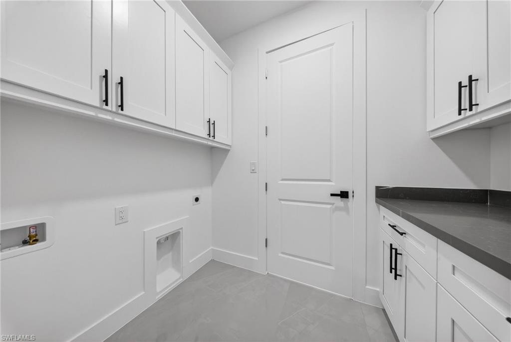 Laundry room featuring extensive white cabinetry, dark countertops, and tile flooring