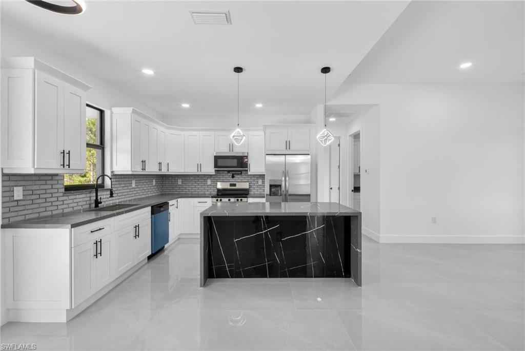 Modern kitchen featuring an expansive center island with a dark stone waterfall countertop, white flat-panel cabinetry with black hardware, an undermount sink with a gooseneck faucet, and stainless steel appliances